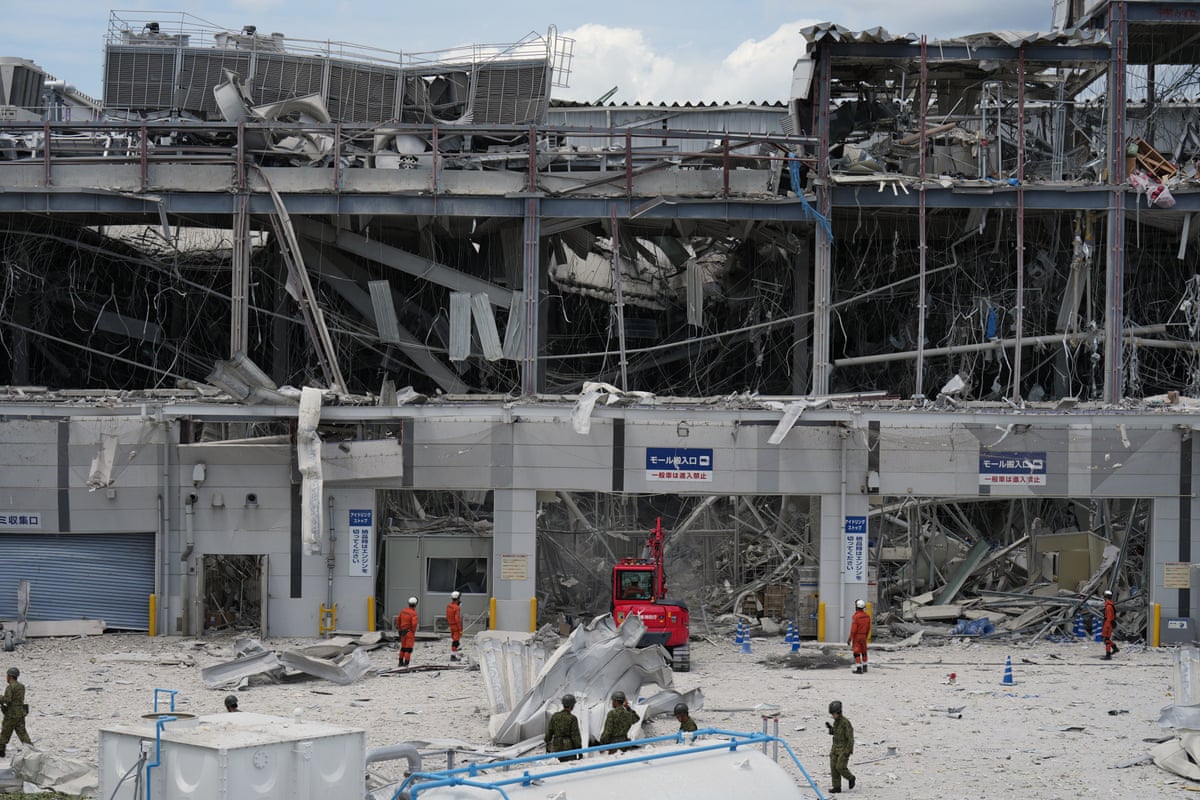 Emergency workers stand near a heavily damaged shopping centre.