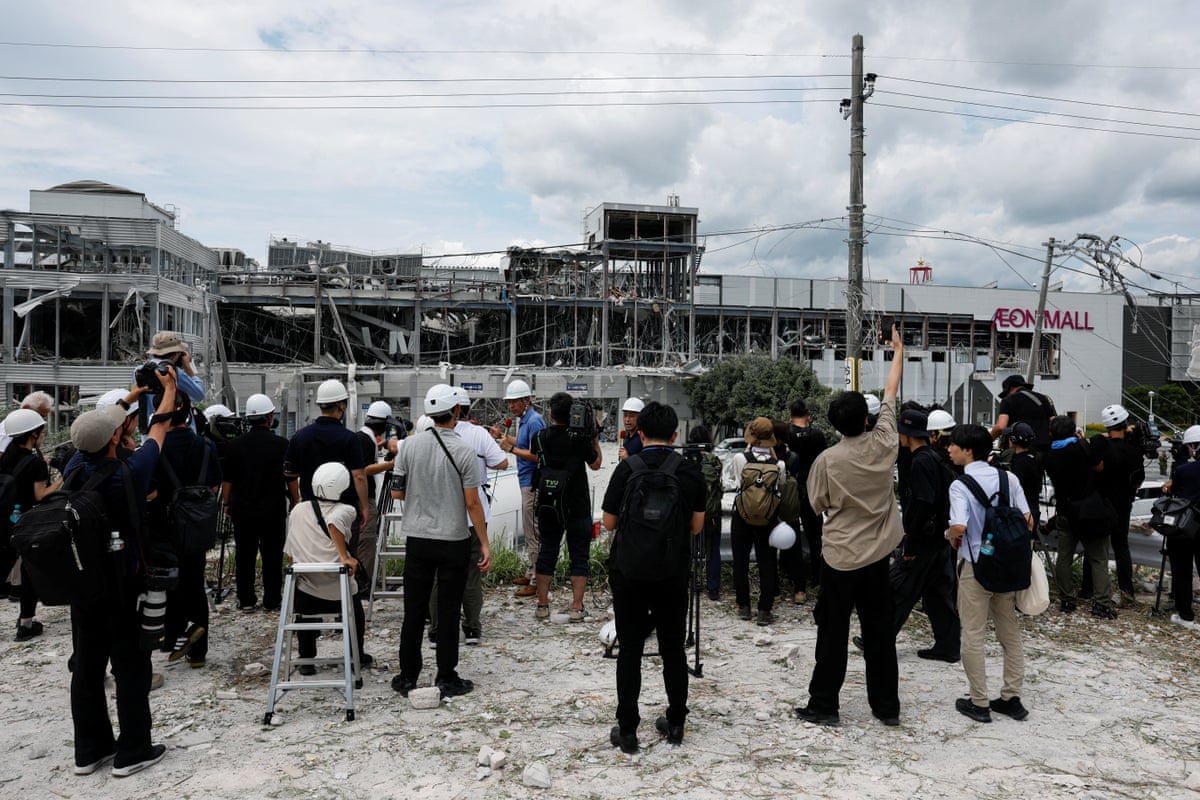 Members of the media stand near the damaged Aeon shopping centre.