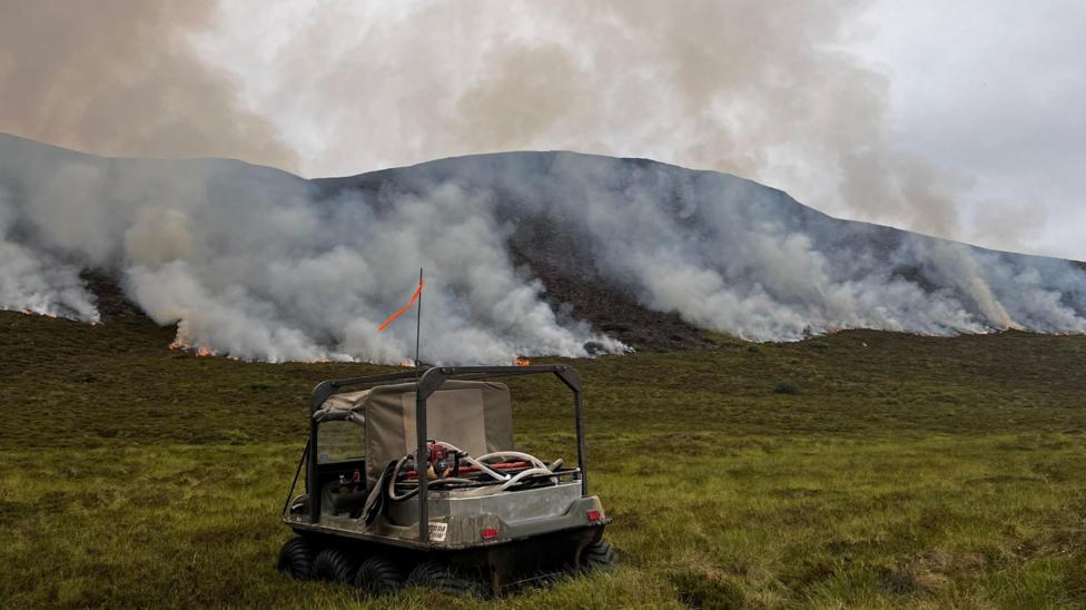 A small all-terrain vehicle with fires burning along a hillside.