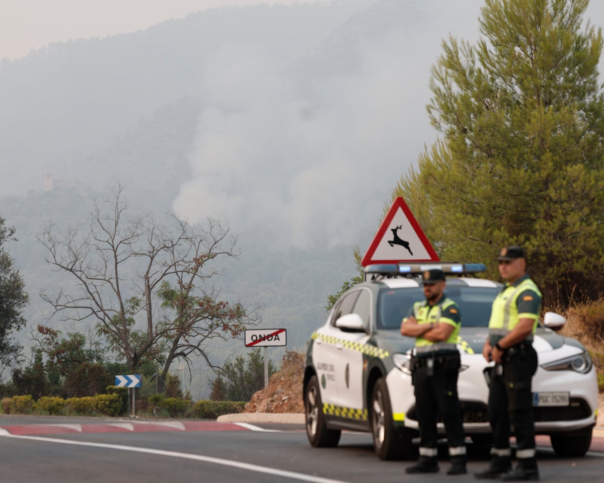 Civil Guards are seen on guard at a closed road as smoke raises from the wild fire very close to the Santa Barbara chapel at La Vall d’Uixo in Castellón, Spain.