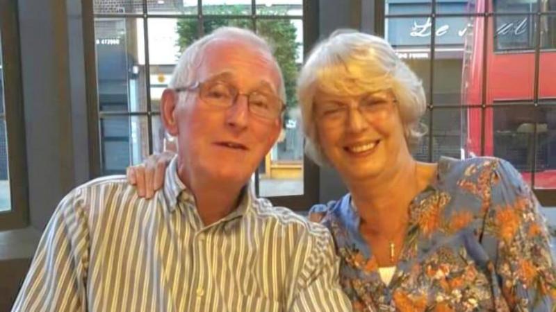 A selfie style shot of John Barrie, a man in his 70s with white hair. His wife Jeanette is next to him wearing black glasses and smiling at the camera.