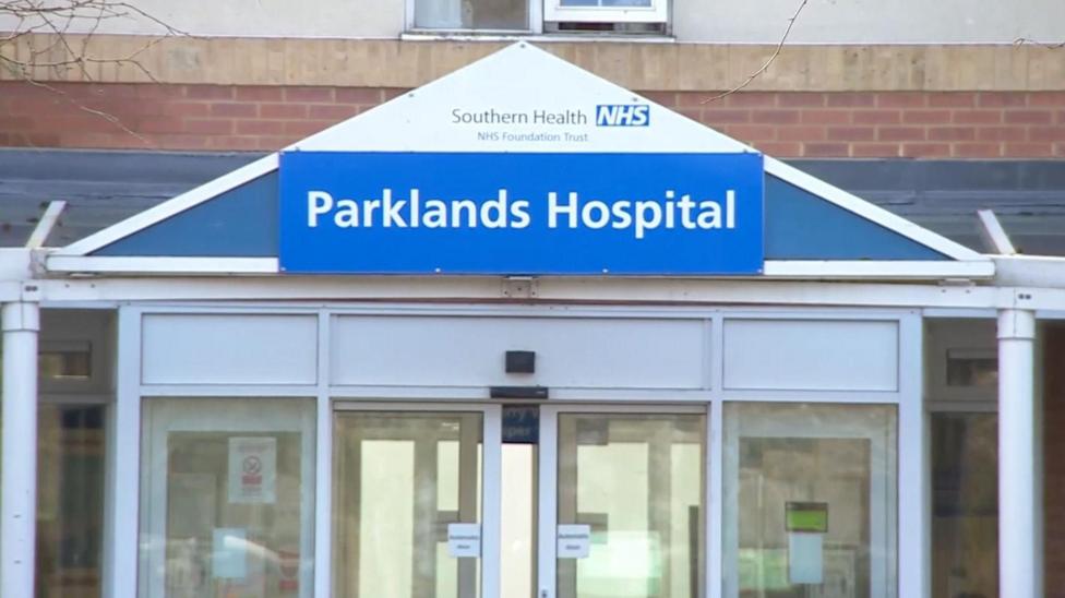 The entrance to Parklands Hospital. The name of the hospital is on a sign above white sliding doors.