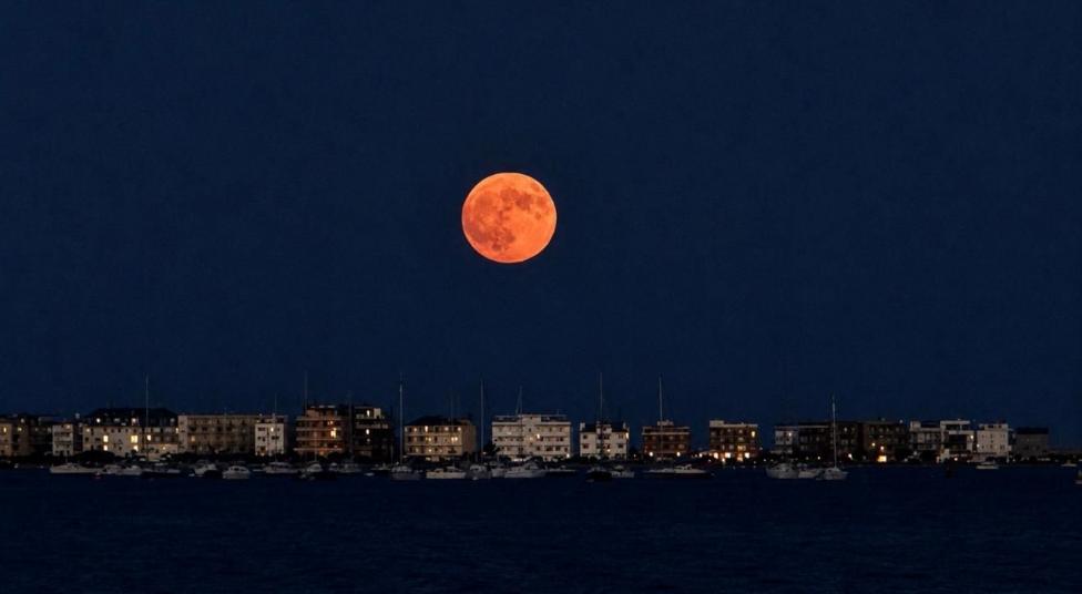 Buck Moon shining above a harbour with small boats and buildings beneath