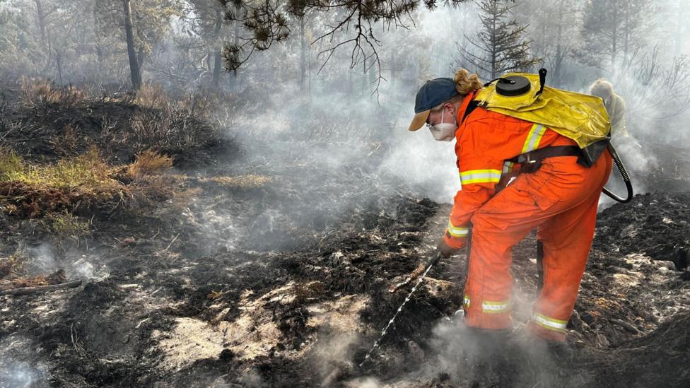 A person wearing orange, protective overalls and wearing a face mask and cap uses water to dampen down hotspots at RSPB Scotland's Loch Garten reserve at Abernethy.