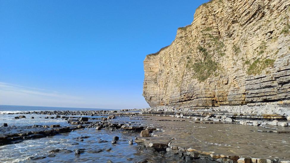 a tall limestone cliff above the sea on a blue sky day