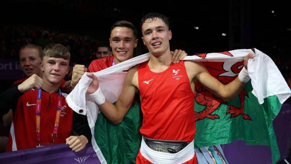 Ioan Croft drapes a flag over his shoulders next to twin brother Garan after winning boxing gold in Birmingham in 2022.