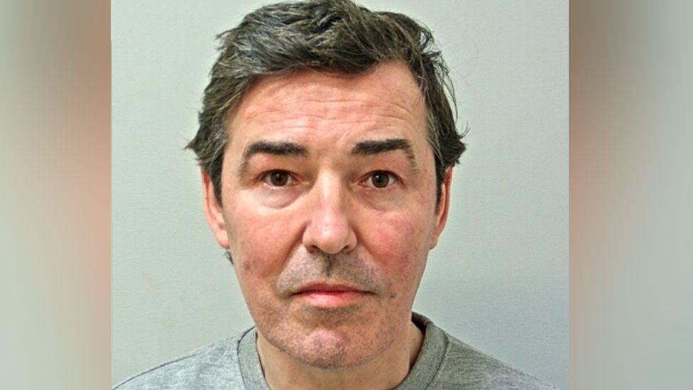 Image shows Darren Davies, who has short dark hair and is wearing a grey prison-issue sweatshirt