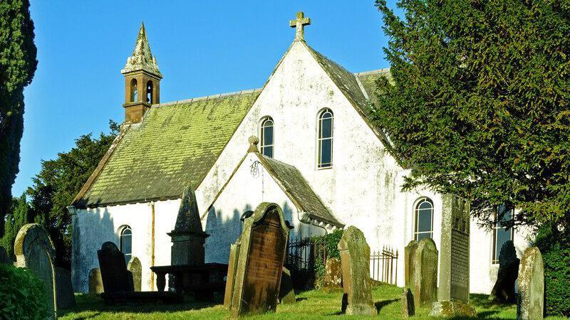 A small white church with gravestones in front of it and trees beside it