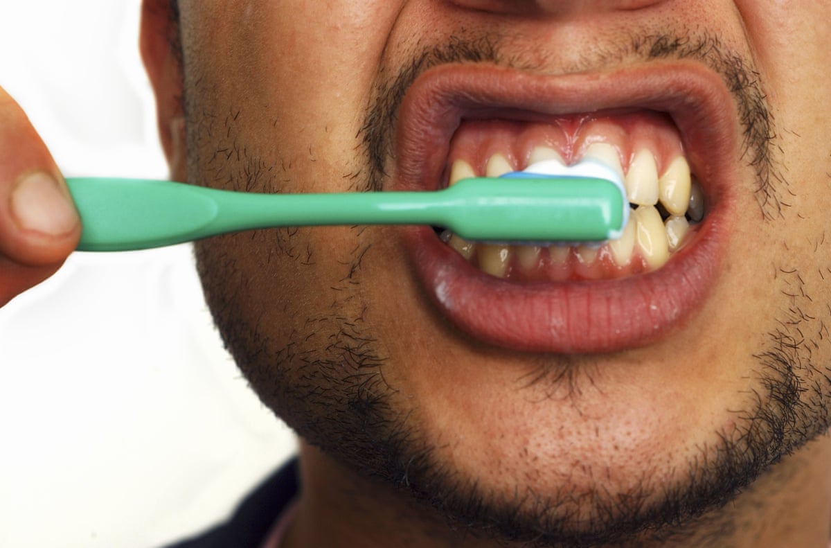 A man brushing his teeth with a green toothbrush