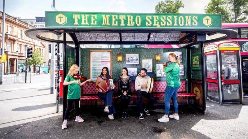 Musicians sat on a bus stop, which has been decorated to appear as a bar. The sign reads 