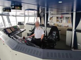 A man in a nautical uniform at the controls of a large ship