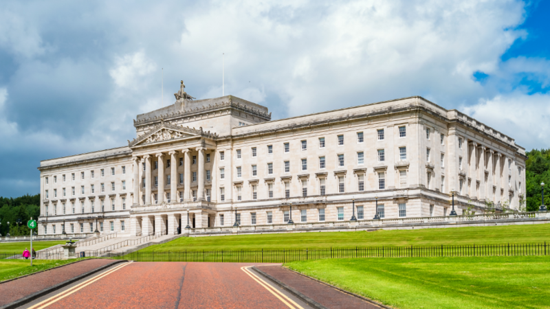 The Northern Ireland assembly building. It is a large white square shape with many windows. There are five large stone pillars at the front door.