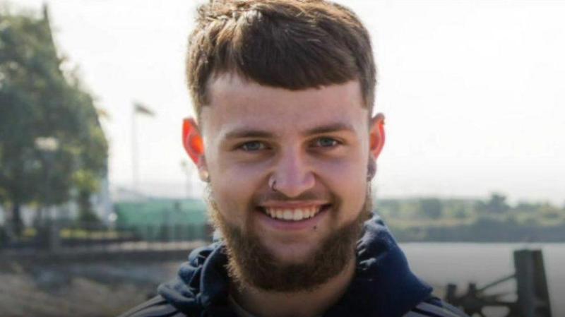 Connor Marshall smiling at the camera. He has short dark hair, a dark beard and has a nose ring.