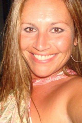Victoria smiling while looking at the camera. She has long brown hair and wears hoop earrings.