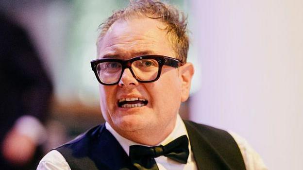 Comedian Alan Carr with his trademark large, dark glasses with a black bow tie, waistcoat and white shirt