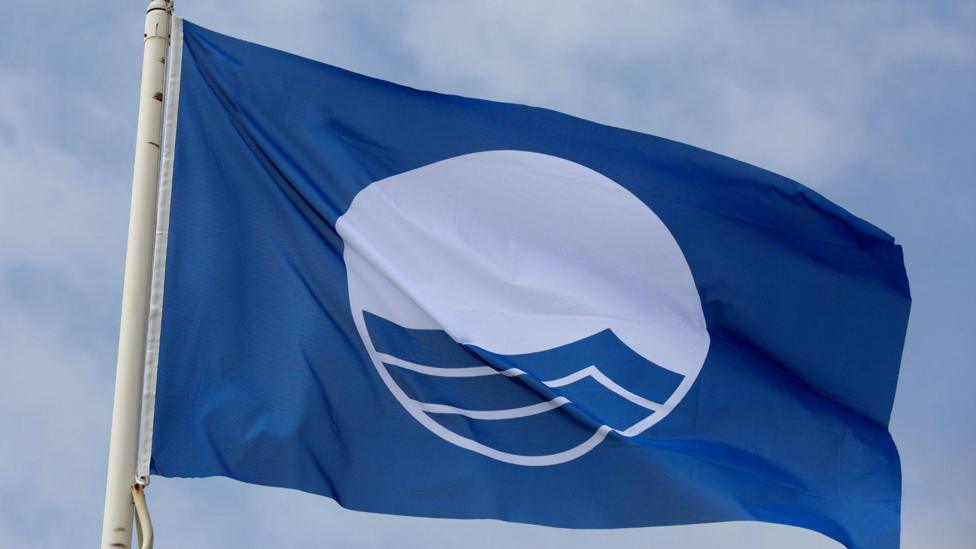 A picture of a Blue Flag flying against a blue sky - the logo on the flag is that of the Blue Flag accreditation scheme