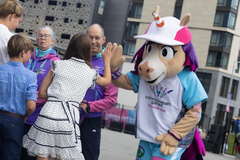 A girl with brown hair and a white polka dot dress high fives a person wearing a unicorn mascot costume