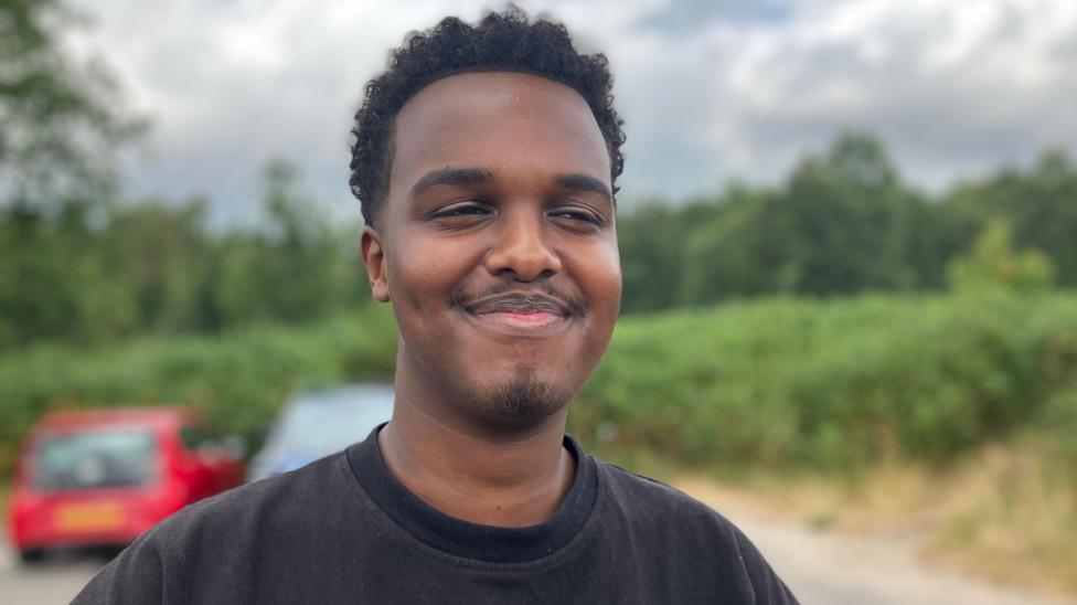 A man stood in a car park wearing a black t-shirt
