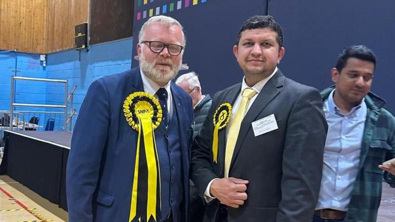 Martyn Day, Falkirk East and Linlithgow, and Dr Zohaib Arshad both wearing rosettes and standing in front of a Falkirk Council backdrop.