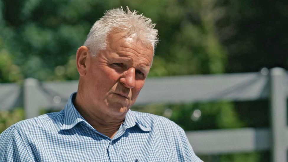 Brian Maywood, who has grey hair and a blue checked shirt, speaks to the BBC in his garden.