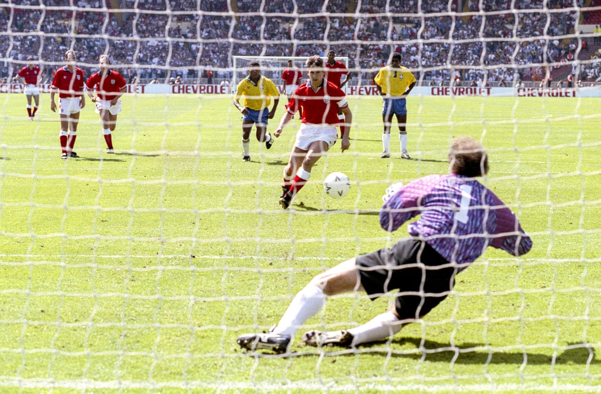 The England striker Gary Lineker takes a penalty which the Brazil goalkeeper Carlos, diving to his right, is about to save easily.