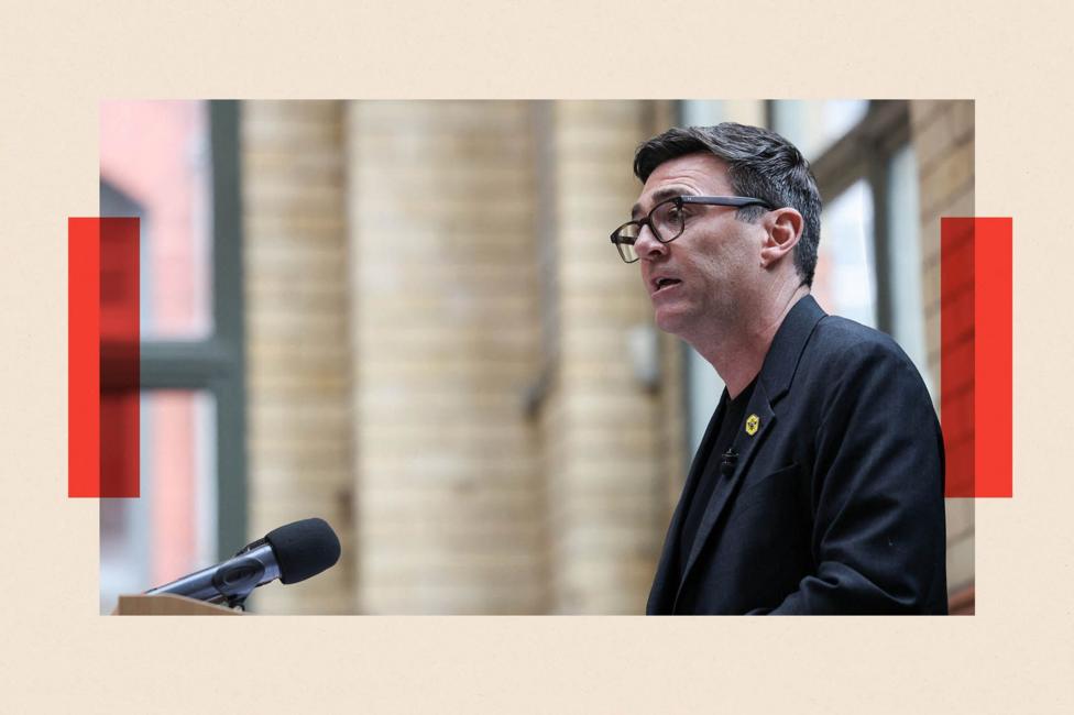 Andy Burnham delivers a speech at the People's History Museum in Manchester. He is viewed in profile standing at a podium. In the background are cream tiles and windows with green frames. Burnham has dark greying hair and wears dark-rimmed glasses and a dark jacket with a bee logo pin badge on his lapel.
