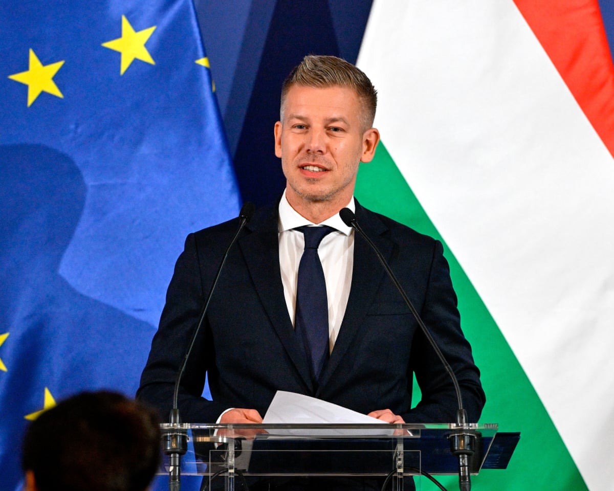 Magyar speaking at a lectern in front of EU and Hungary flags