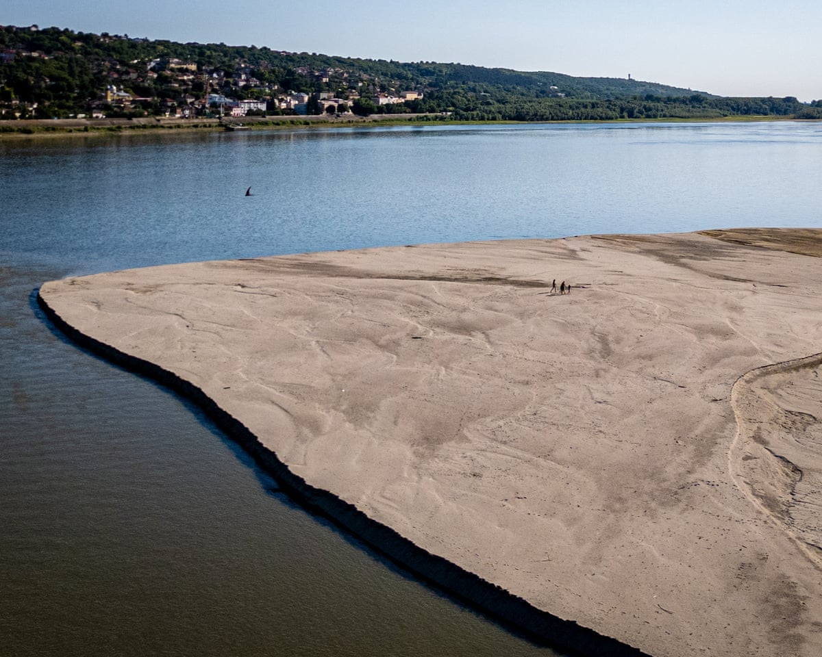 People walk on a bank of sand on the Danube River as usually submerged areas are exposed due to extreme low levels of the water following an extended period of drought in Oltenita, Romania.
