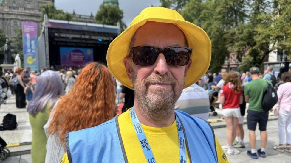 Kevin McVeigh, a man with a yellow hat, dark glasses, a beard, yellow t-shirt and also wearing a blue bib.