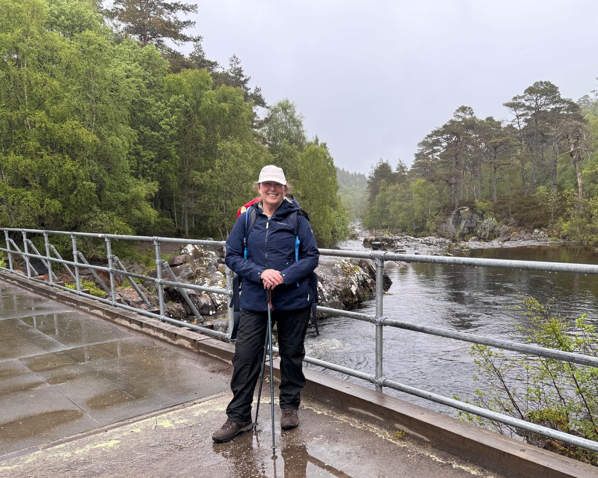 Female hiker with walking poles on a bridge over a river on a wet day