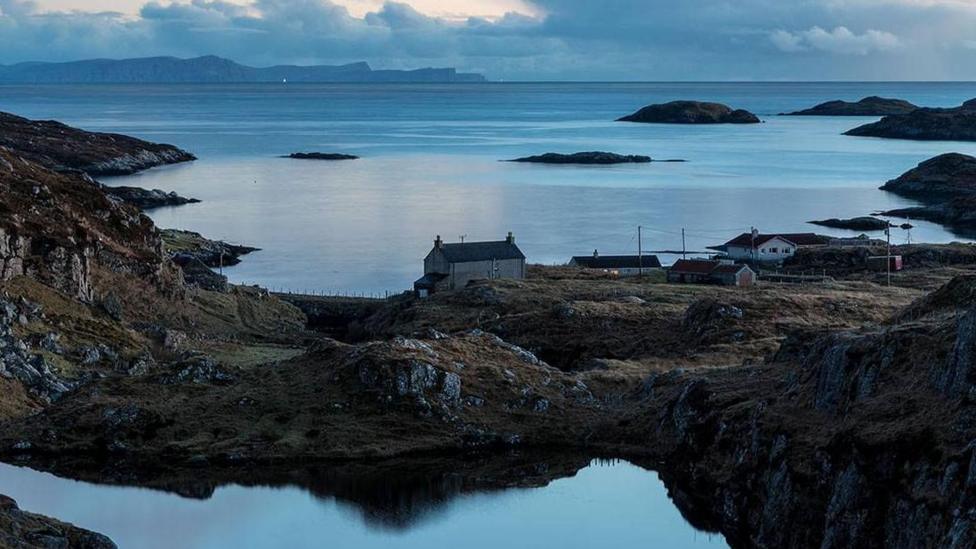 A view across a landscape of lochs and rocky coast, dotted by a few houses in Bays of Harris in the Western Isles.