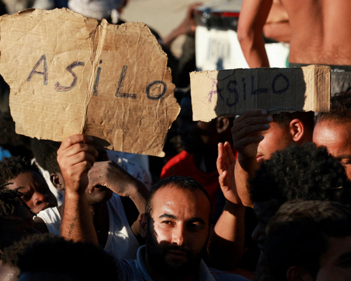 Migrants hold signs reading