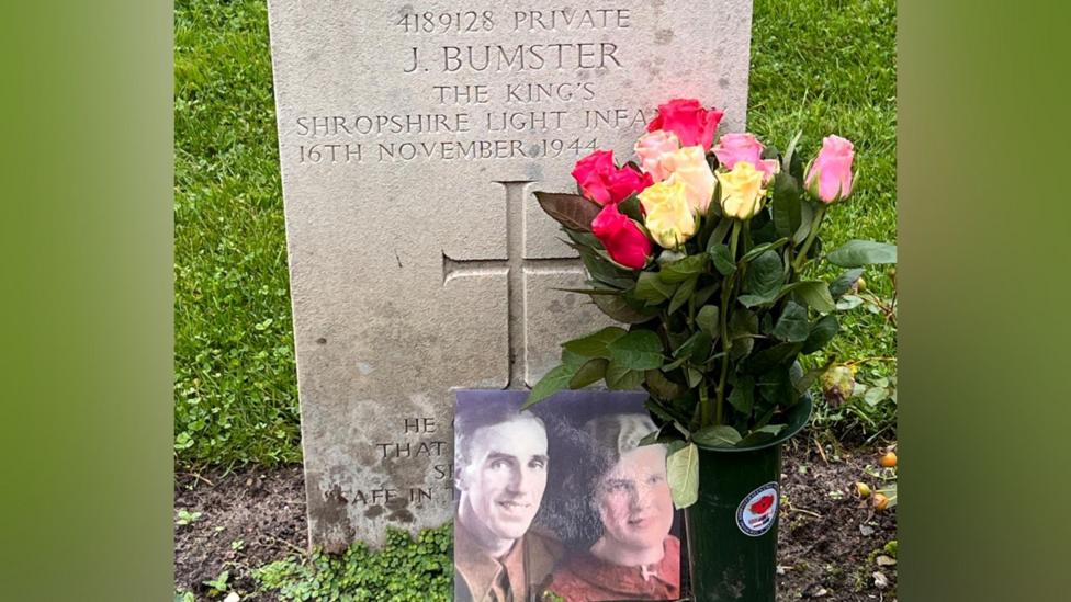 A picture of James Bumster's grave in Venray, the Netherlands. There is a photograph of him and his wife on the grave, along with pink and white roses.