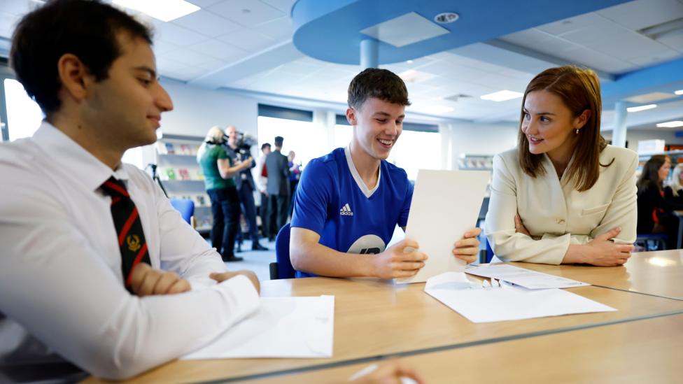 Education Secretary Màiri McAllan sitting at a table with students who have just received their exam results