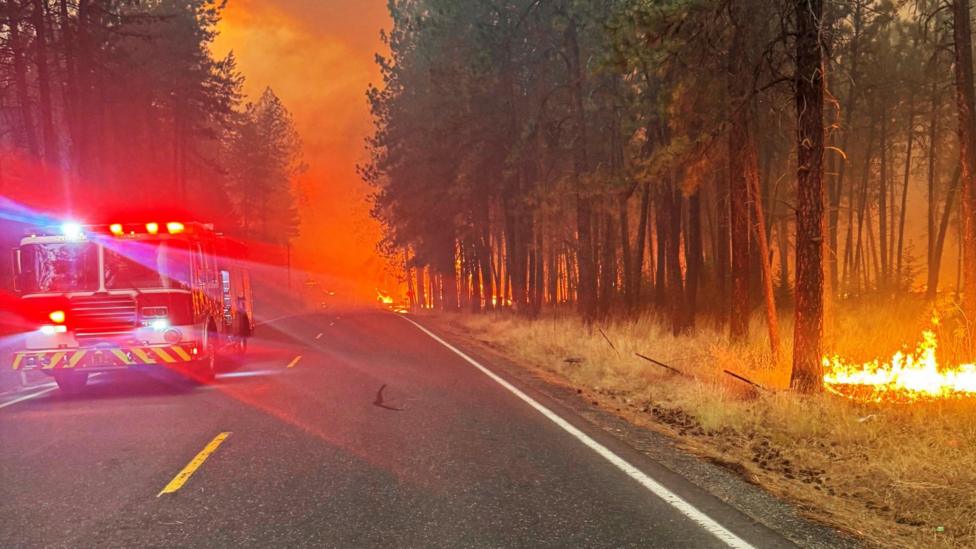 A Spokane Valley Fire Department truck on the road, surrounded by burning trees
