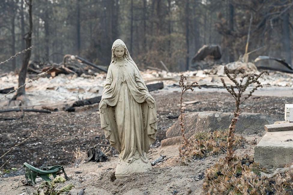 A Virgin Mary statue stands alone amid a field of charred debris