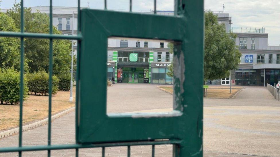 A school building in the background, looking through a green gate in the foreground.