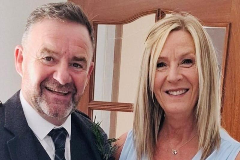 Harry Grieve and Kim Hutchison, a couple smiling to the camera, he is wearing a tartan tie and white shirt, she is wearing a light blue dress. He has short, grey hair and a beard and she has mid-length blonde hair.