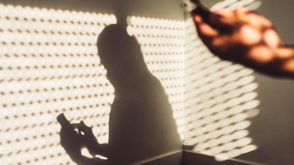 Shadow of a woman using a smartphone at home.