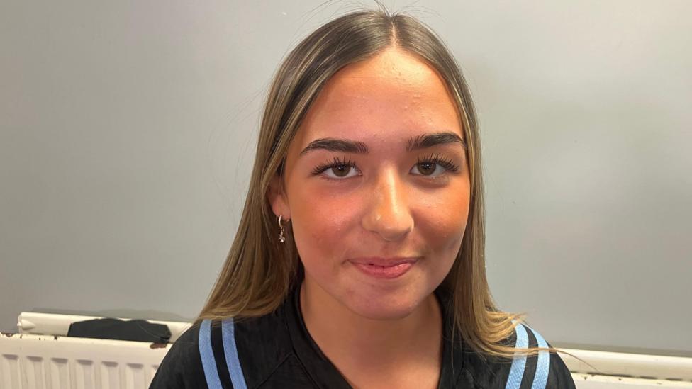Cora Nelis has long fair hair and is wearing a navy and light blue sports top