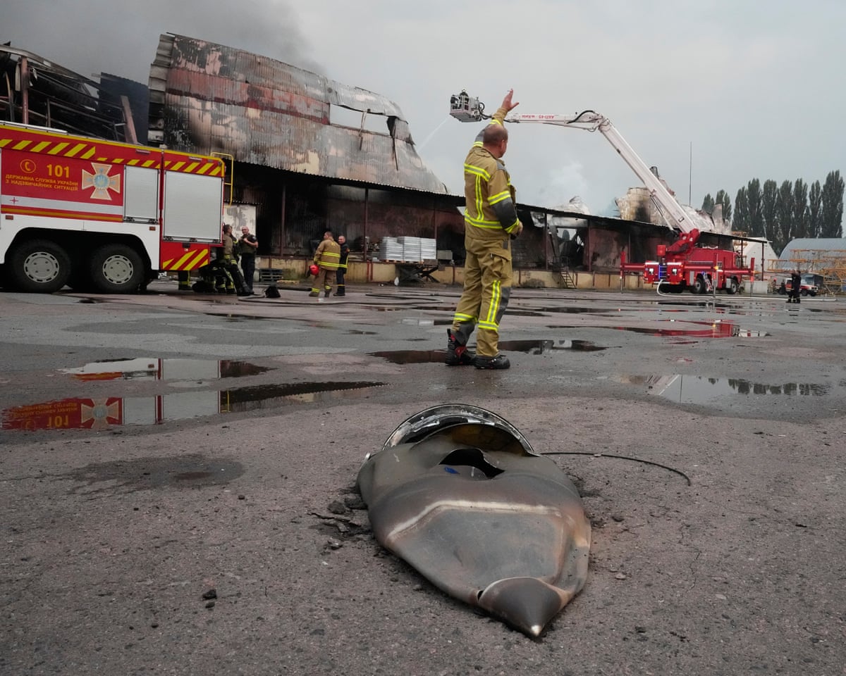 A firefighter stands near a fragment of a Russian missile with a fire engine behind him