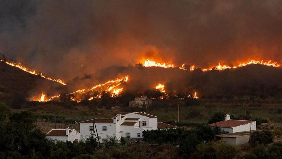 Flames tear through the hills around houses.