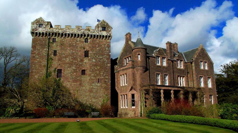 A side view of Comlongon Castle with the Tower House and mansion beside it with sweeping lawns in front