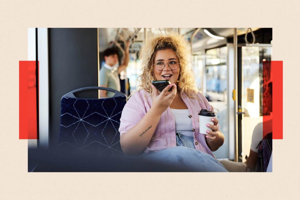 A woman using her mobile on speakerphone on a bus while holding a coffee