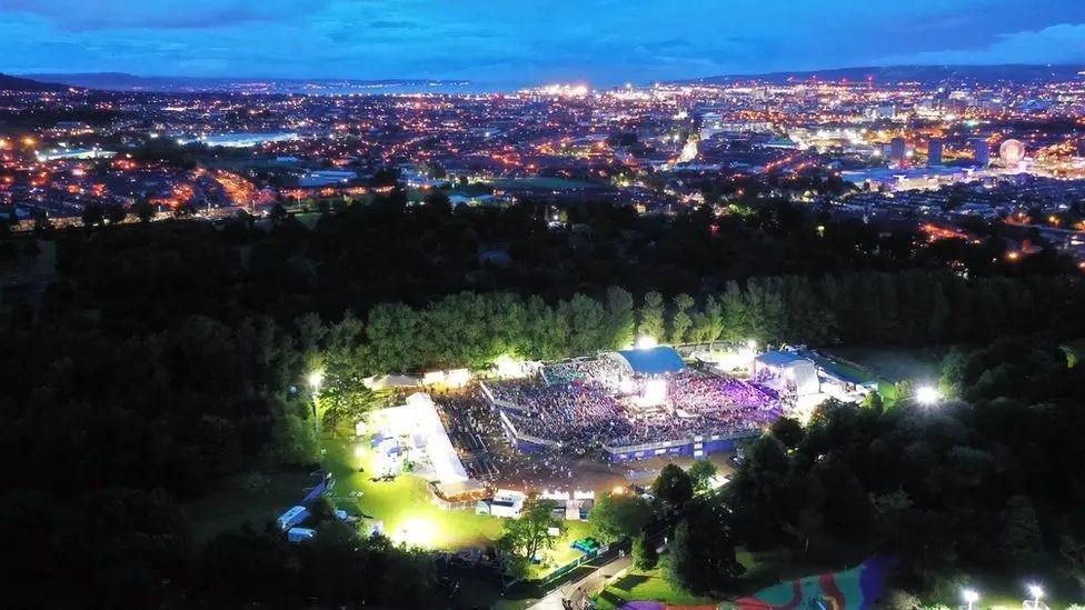 Crowds at a night concert at Falls Park. There are trees beside the venue and bright lights around it