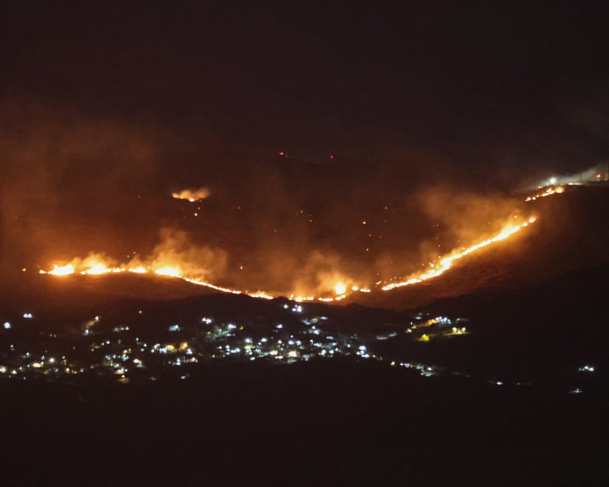 Flames sweeping across a forested hillside above a village.