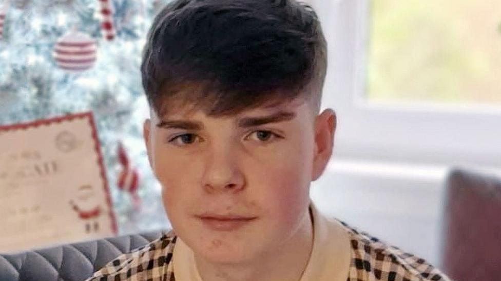Kayden Moy looks in the camera and smiles - he is a teenage boy with short dark hair.