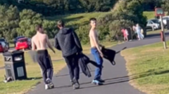 A blurry CCTV image of the three killers of Kayden Moy walking through a park on a sunny day. Two have their backs to the camera, while Stewart is looking backwards, and into the camera. Two of the three are shirtless.