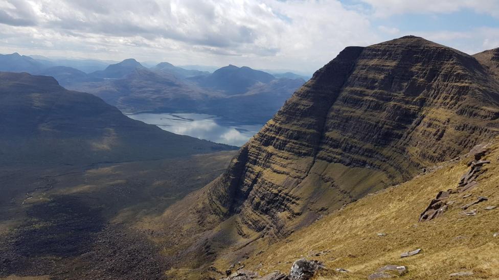 A stunning view over a landscape of mountains and a loch. In the foreground is the mountain Beinn Alligin.