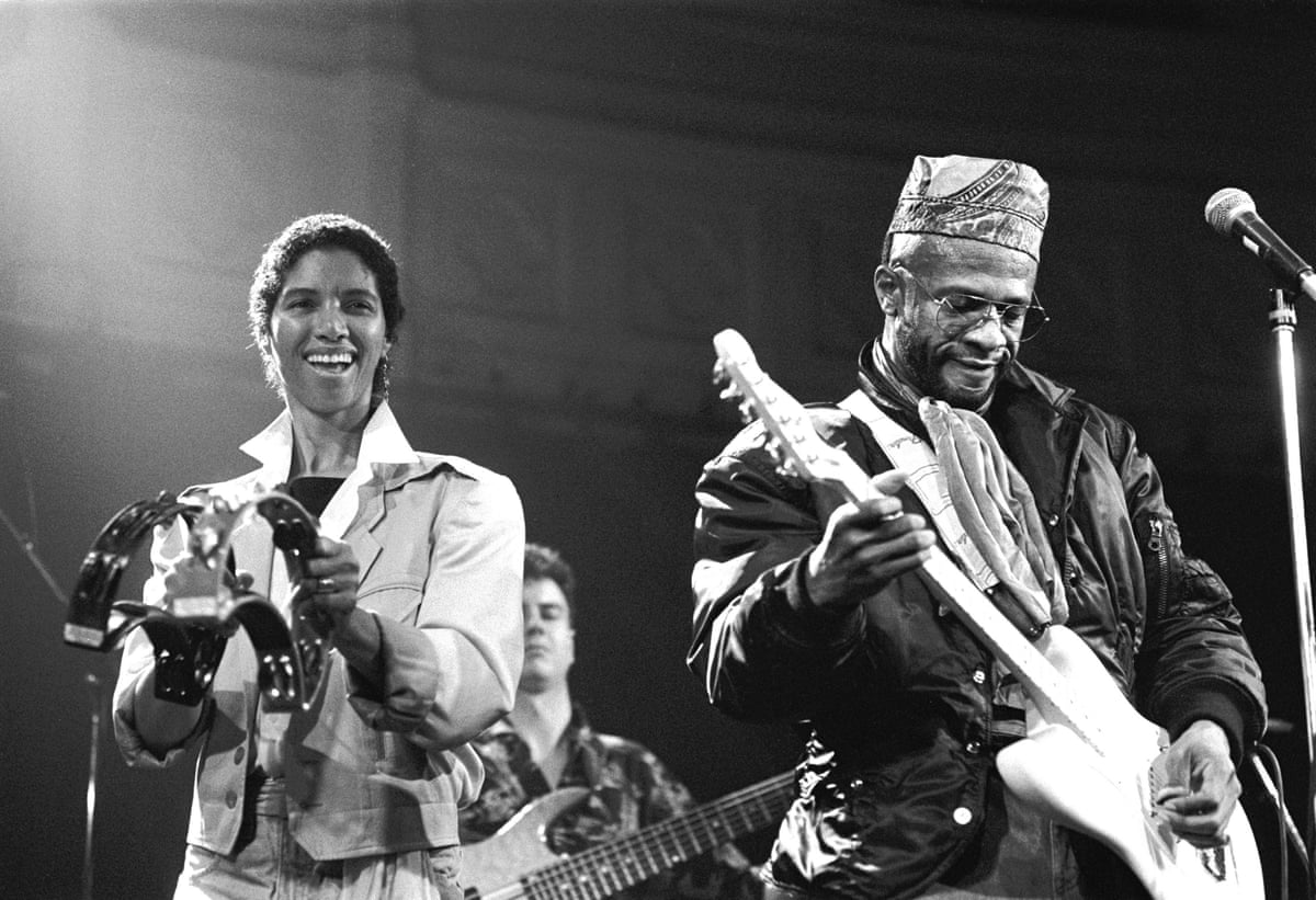 Linda, smiling, bangs a tambourine while Cecil plays an electric guitar